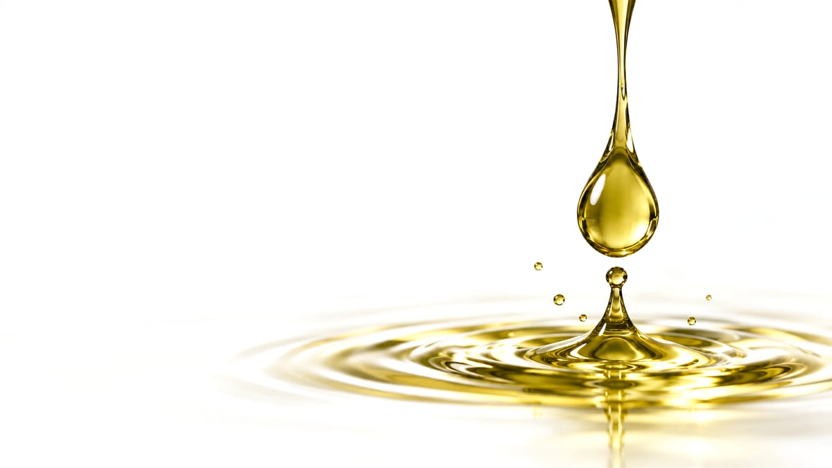 A drop of golden oil falling into a pool of oil, raising a small splash and ripples